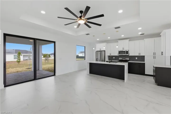 Kitchen with dark cabinets, white cabinets, an island with sink, decorative light fixtures, and decorative backsplash