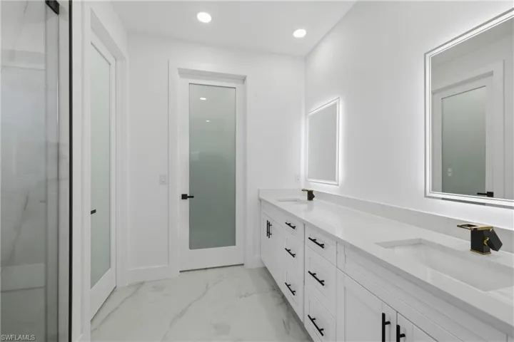 Bathroom featuring recessed lighting, double vanity, light marble finish flooring, and a shower with door
