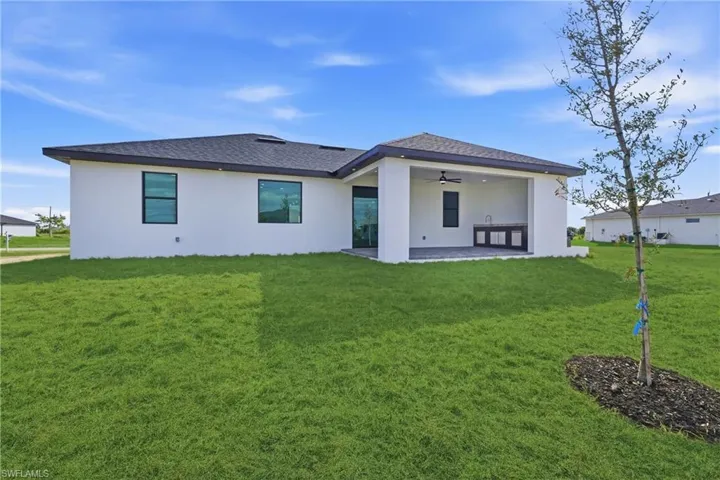 Rear view of property with stucco siding, ceiling fan, and a yard