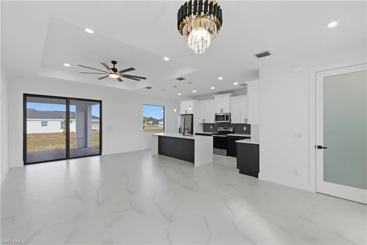 Kitchen with open floor plan, a kitchen island with sink, white cabinets, stainless steel appliances, and tasteful backsplash