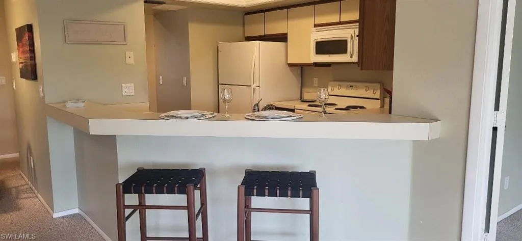 Kitchen featuring a breakfast bar area, light countertops, white appliances, a peninsula, and baseboards