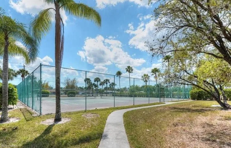 View of tennis court with fence and a lawn