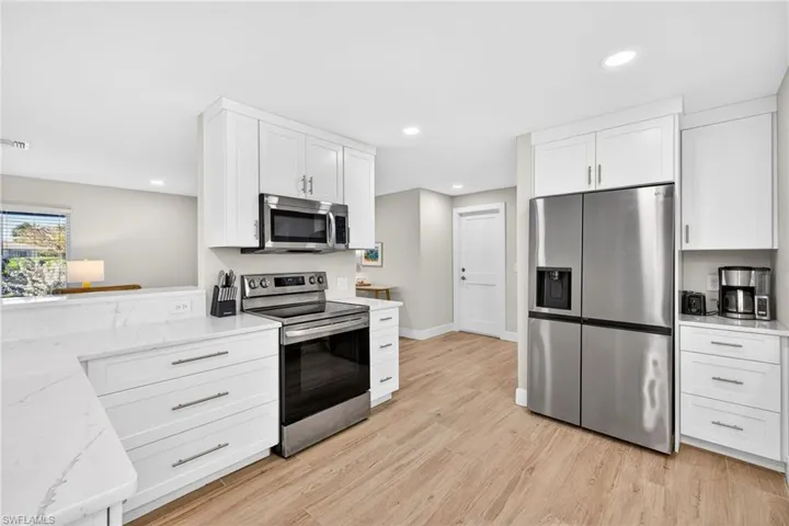 Kitchen with stainless steel appliances, white cabinetry, light wood-style flooring, light stone counters, and recessed lighting