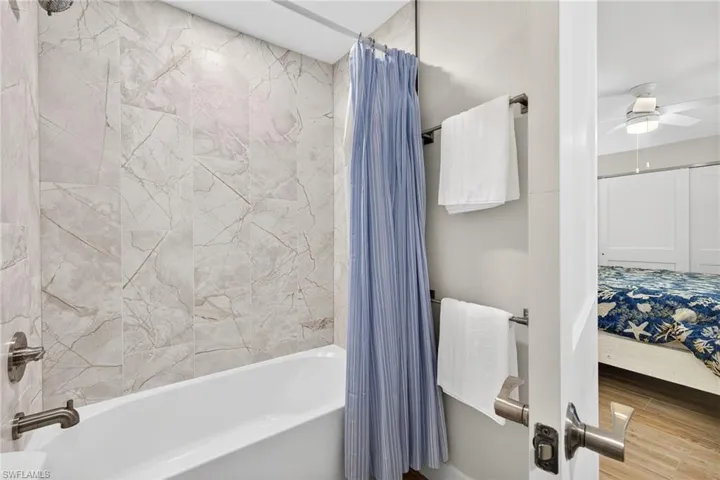 Bathroom featuring shower / bathtub combination with curtain, ensuite bath, a ceiling fan, and wood finished floors