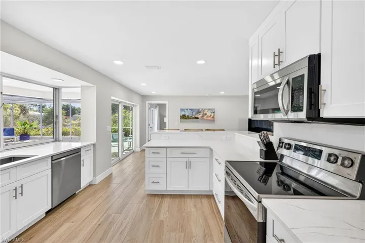 Kitchen with stainless steel appliances, a peninsula, white cabinets, light stone counters, and recessed lighting