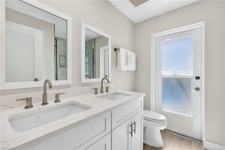 Bathroom with double vanity, light wood finished floors, and a shower with door