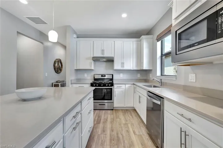 Kitchen featuring stainless steel appliances, decorative light fixtures, sink, light hardwood / wood-style floors, and white cabinets