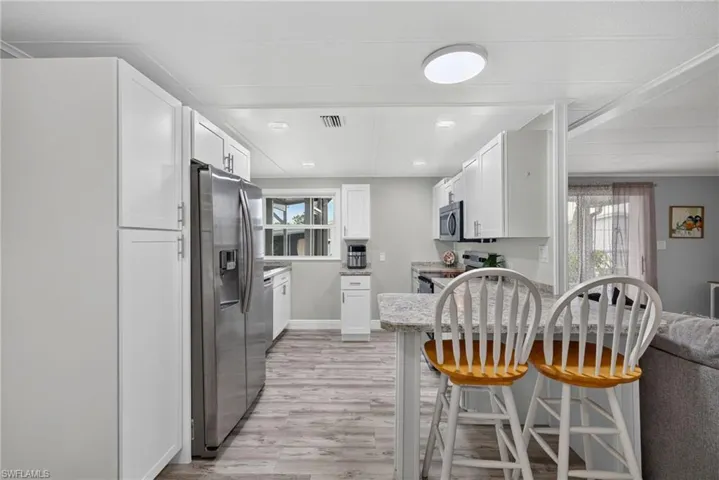 Kitchen featuring white shaker-style cabinetry, stone-patterned countertops, wood-finish flooring, stainless steel refrigerator, and recessed ceiling lighting