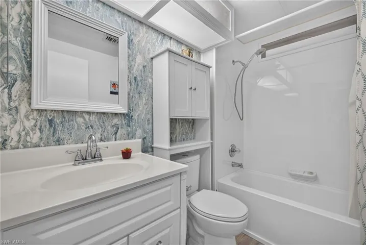 Bathroom featuring a white vanity with an integrated basin, chrome-finish faucet, built-in over-the-toilet cabinetry, and a shower-tub combination with a wall-mounted hand shower