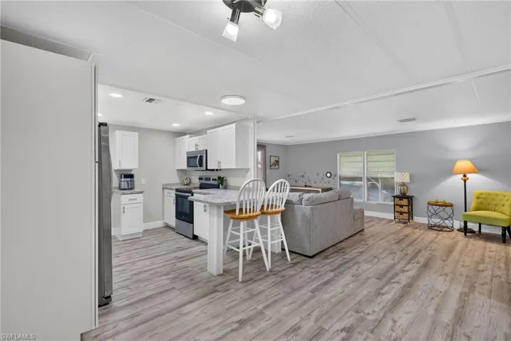 Kitchen featuring white cabinetry, stone-finish countertops, stainless steel appliances, and an integrated breakfast bar, complemented by wood-finish flooring throughout the open-concept space