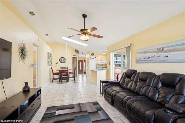 Living room featuring light tile patterned floors, visible vents, vaulted ceiling with skylight, and ceiling fan