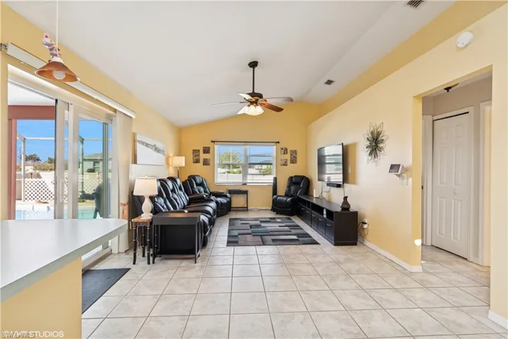 Living area with light tile patterned floors, visible vents, lofted ceiling, and ceiling fan