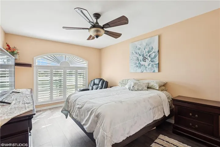 Bedroom with Plantation Blinds wood finished floors, ceiling fan