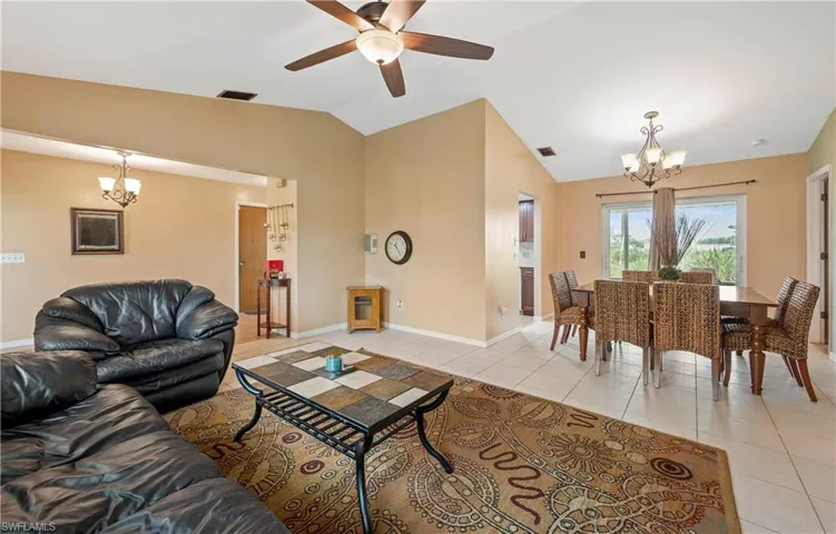 Living area featuring a chandelier, lofted ceiling, light tile patterned floors, a ceiling fan, and baseboards