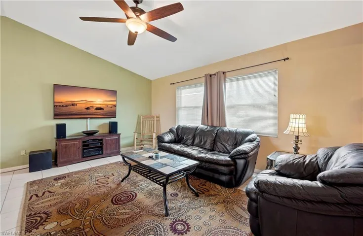 Tiled living room with vaulted ceiling, ceiling fan, and baseboards