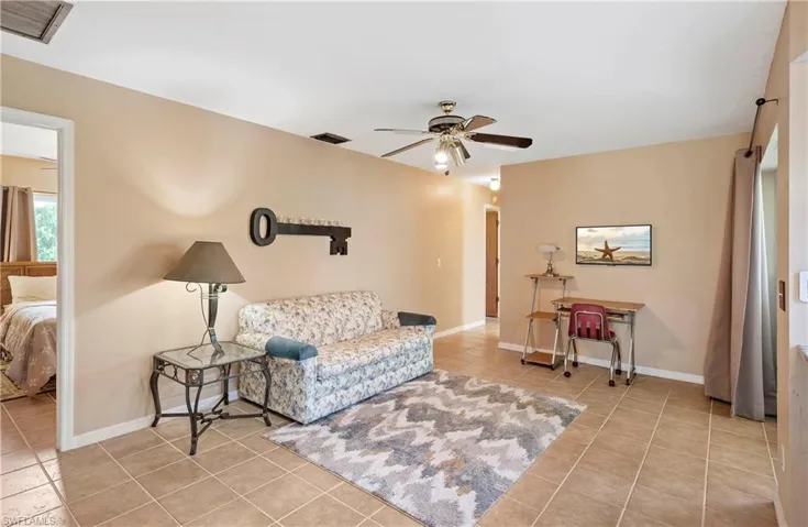 Tiled living area featuring ceiling fan and baseboards