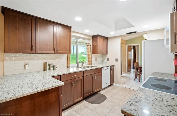 Kitchen with white dishwasher, a sink, decorative backsplash, light tile patterned floors, and light stone countertops