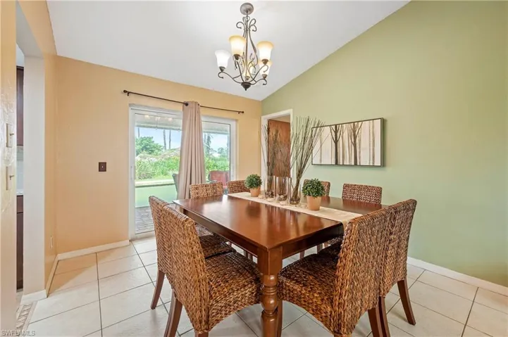 Dining room featuring a chandelier, vaulted ceiling, baseboards, and light tile patterned flooring