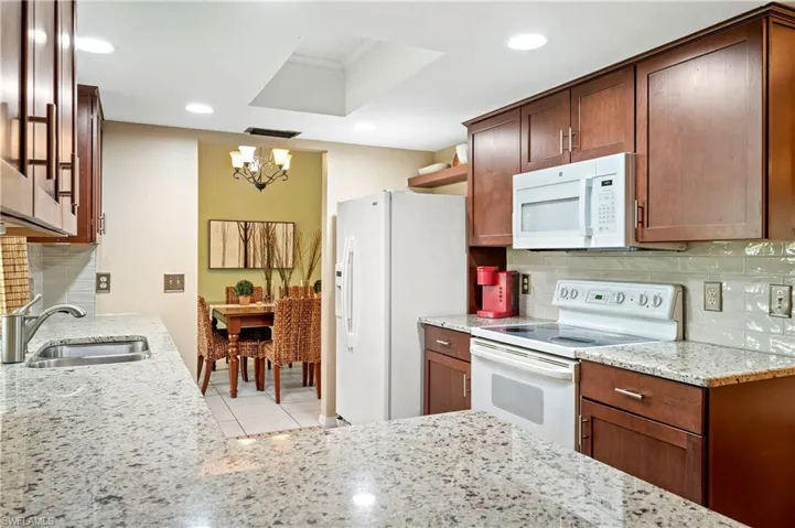 Kitchen featuring white appliances, a chandelier, a sink, light stone counters, and recessed lighting