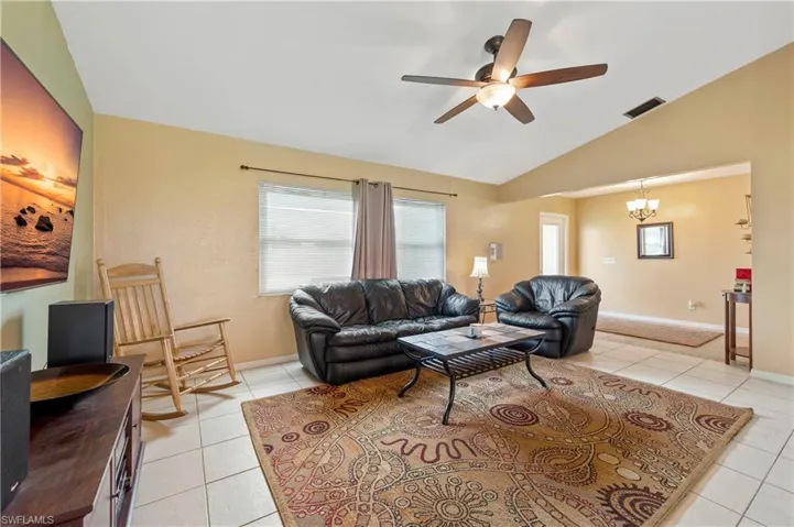 Living room featuring light tile patterned floors, a ceiling fan, plenty of natural light, a chandelier, and lofted ceiling