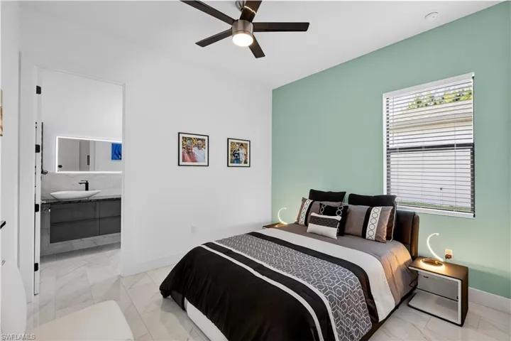 Guest bedroom with a ceiling fan, light marble finish flooring, and connected bathroom