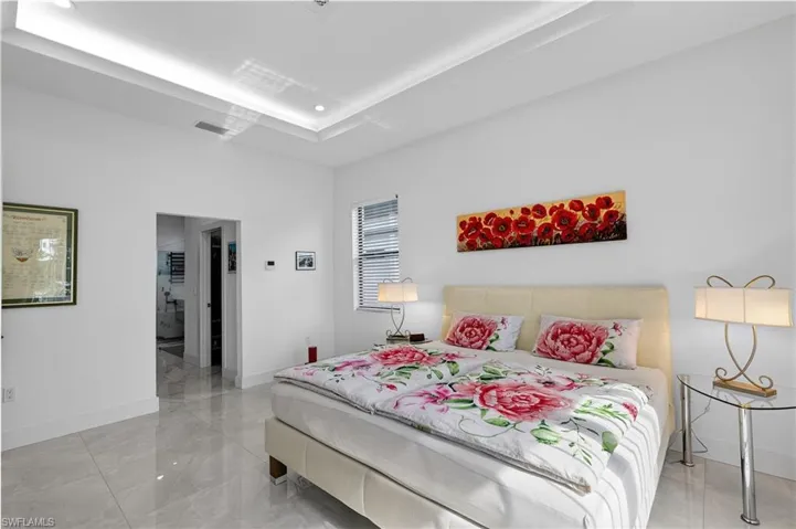 Bedroom with light marble finish flooring, a tray ceiling, and connected bathroom