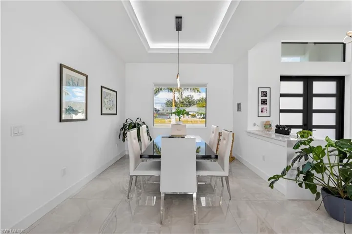 Dining space featuring a tray ceiling, light marble finish floors, and a chandelier
