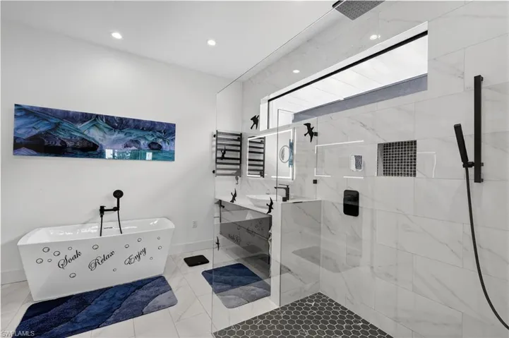 Master bathroom featuring vanity's, a freestanding bath, a marble finish shower and a towel warmer