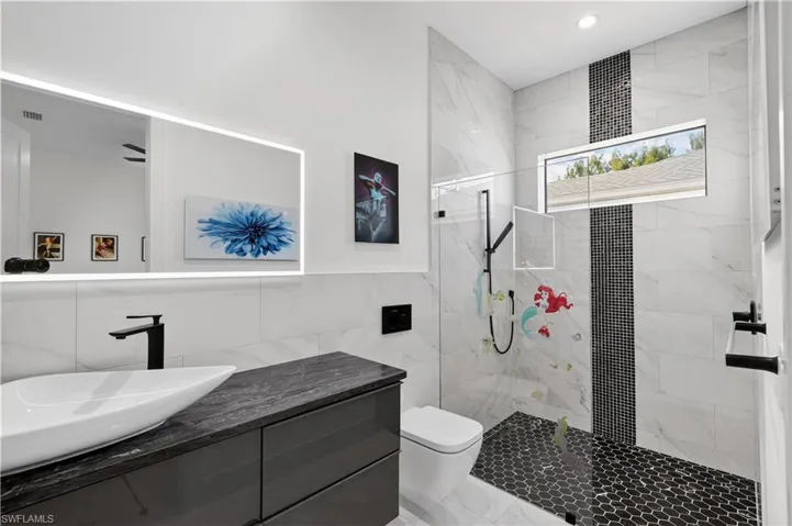 Full bath with vanity, a marble finish shower, and tile walls