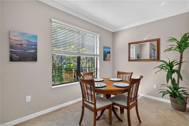Neutral-toned walls featuring crown molding, ceramic tile flooring, and a large window with muntin Dining area with easy access to kitchen and living area.