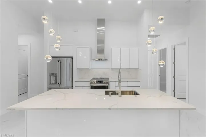 Kitchen with decorative backsplash, sink, hanging light fixtures, appliances with stainless steel finishes, and white cabinets