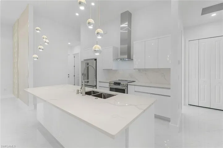 Kitchen with hanging light fixtures, a kitchen island with sink, wall chimney exhaust hood, and stainless steel appliances