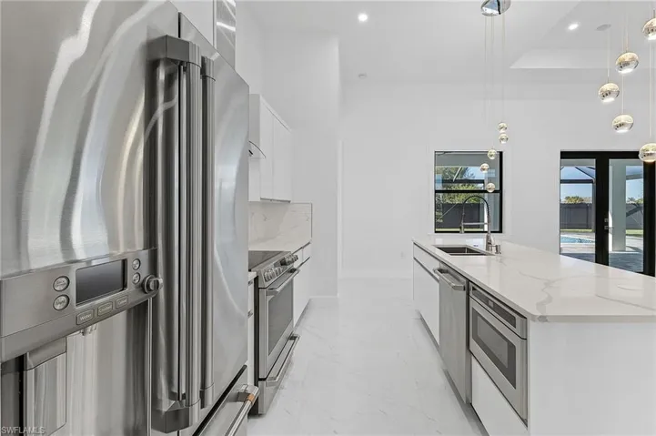 Kitchen with pendant lighting, a large island with sink, white cabinetry, stainless steel appliances, and sink