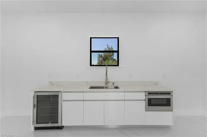 Kitchen with white cabinetry, wall oven, beverage cooler, light stone counters, and sink