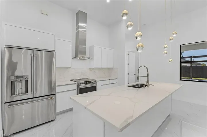 Kitchen featuring appliances with stainless steel finishes, wall chimney range hood, white cabinets, and sink