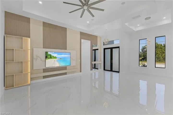 Unfurnished living room with ceiling fan with notable chandelier, a tray ceiling, built in features, and french doors