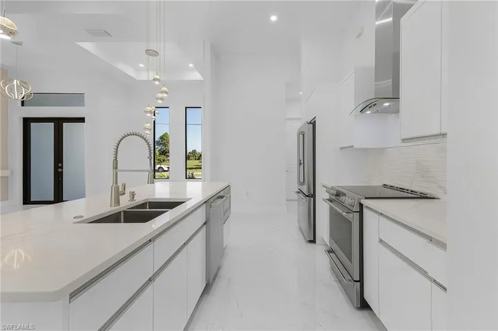 Kitchen with decorative light fixtures, white cabinets, wall chimney range hood, and stainless steel appliances