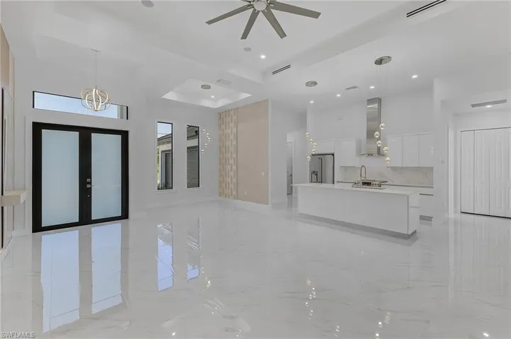 Unfurnished living room featuring ceiling fan with notable chandelier, sink, a tray ceiling, and french doors