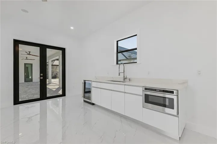 Kitchen featuring beverage cooler, oven, light stone countertops, white cabinets, and sink