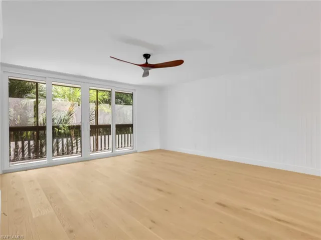 Hardwood-style flooring, white paneled wall, multi-panel sliding glass doors, built-in ceiling fan, and outdoor railing