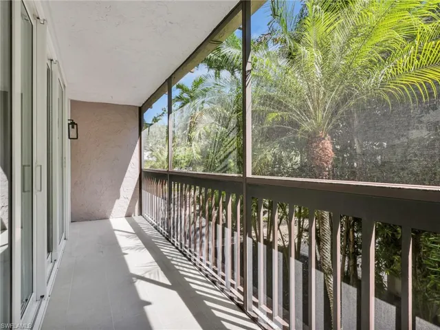 Screened balcony with light-colored tile flooring, white sliding glass doors, and a dark wall lantern