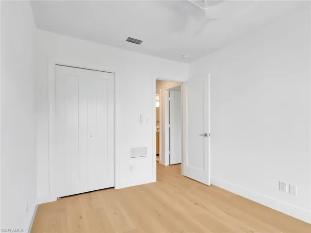 Light wood-finish flooring, white walls, and a white ceiling fan