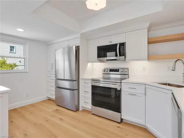 White cabinetry, stainless steel appliances, wood-finish flooring, undermount sink, and recessed lighting