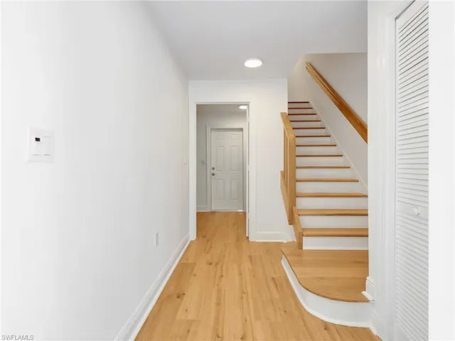 Recessed lighting, wood-finish flooring, wood staircase with natural wood handrail, white interior doors, and louvered closet doors