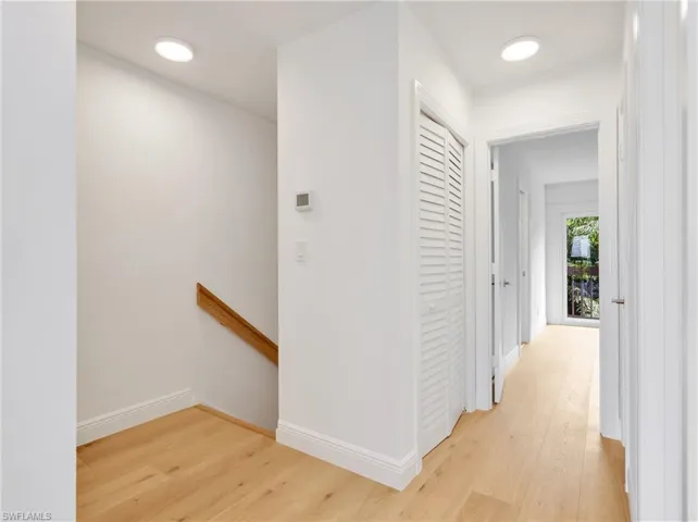 Recessed lighting, wood-finish flooring, white louvered closet doors, wood handrail, and white wall finishes