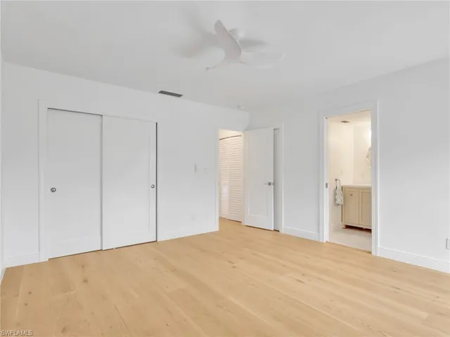 Wood-finish flooring, white walls, white sliding closet doors, a contemporary ceiling fan, and a light wood-finish vanity with a white countertop