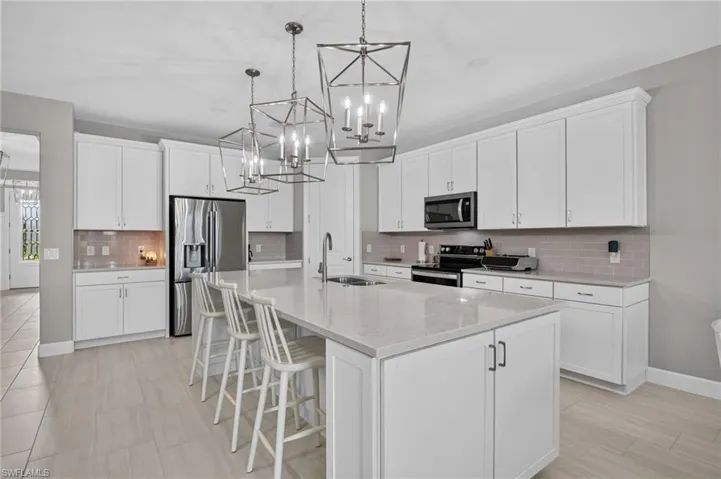 Modern kitchen featuring a large center island with integrated sink, white cabinetry with dark hardware, and a subway tile backsplash