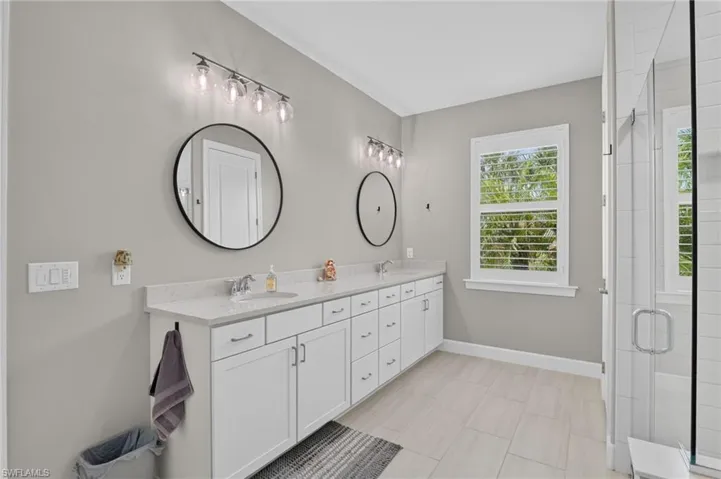 Dual vanity with white cabinetry, quartz countertops, and round black-framed mirrors