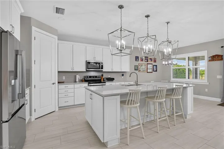 Spacious kitchen featuring white cabinetry, light countertops, stainless steel appliances, a center island with sink, and three geometric pendant lights
