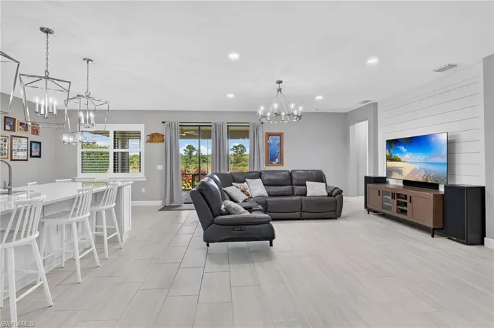 Open-concept interior featuring light plank-style flooring, a kitchen island with seating, pendant lighting, recessed ceiling lights, and a shiplap-accented wall